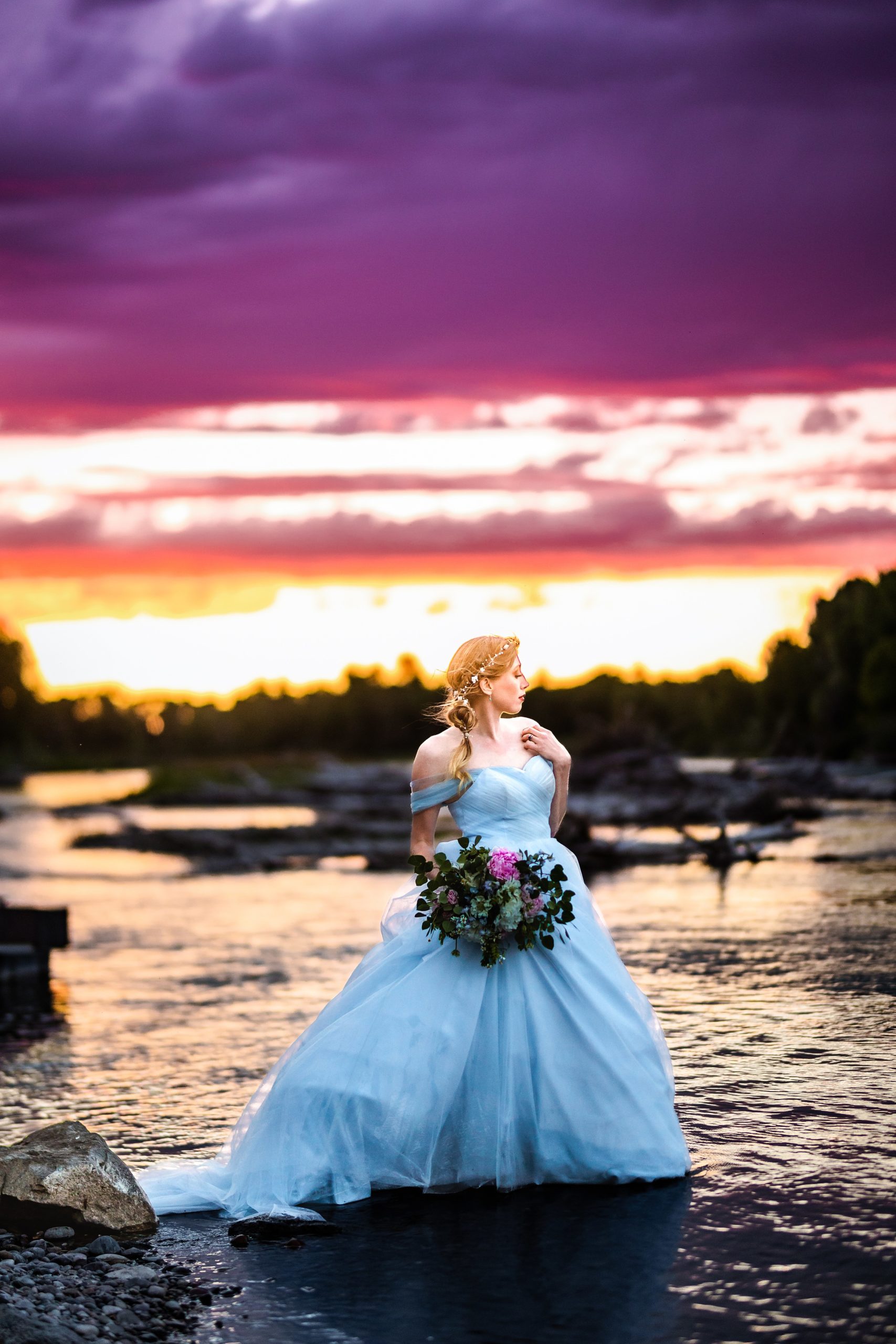 Purple sky bride in blue dress with orange and pink sunset next to beautiful river