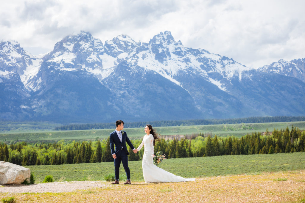 bride and groom walking hand in hand through mountain view turnout at grand teton elopement