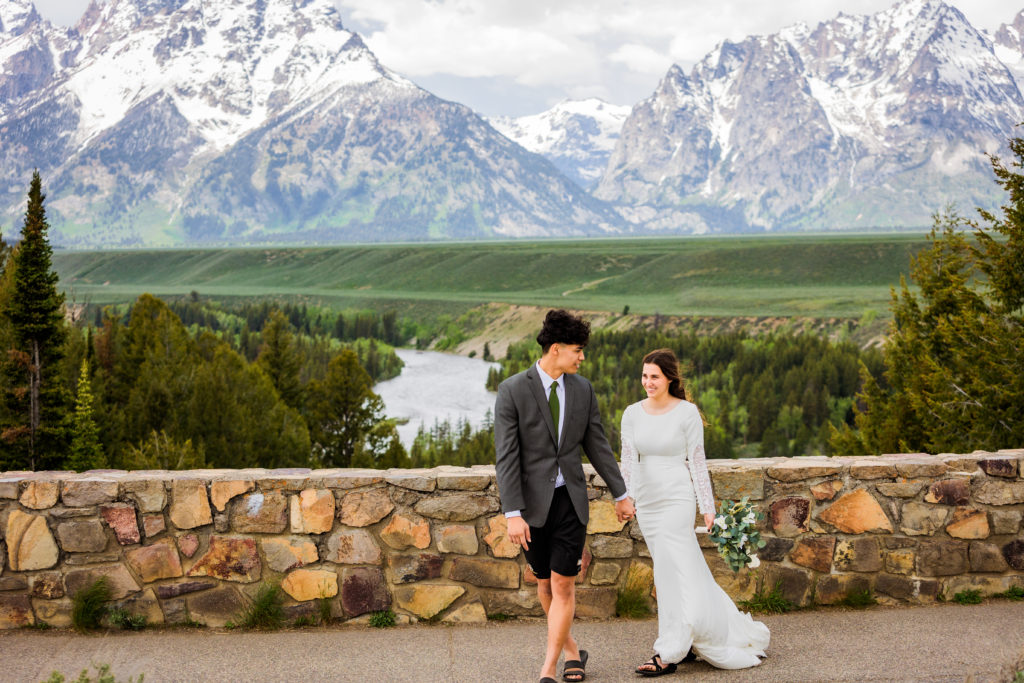 Grand Teton wedding with bride and groom holding hands and walking together at Snake River Overlook in the Tetons taken by wedding photographers