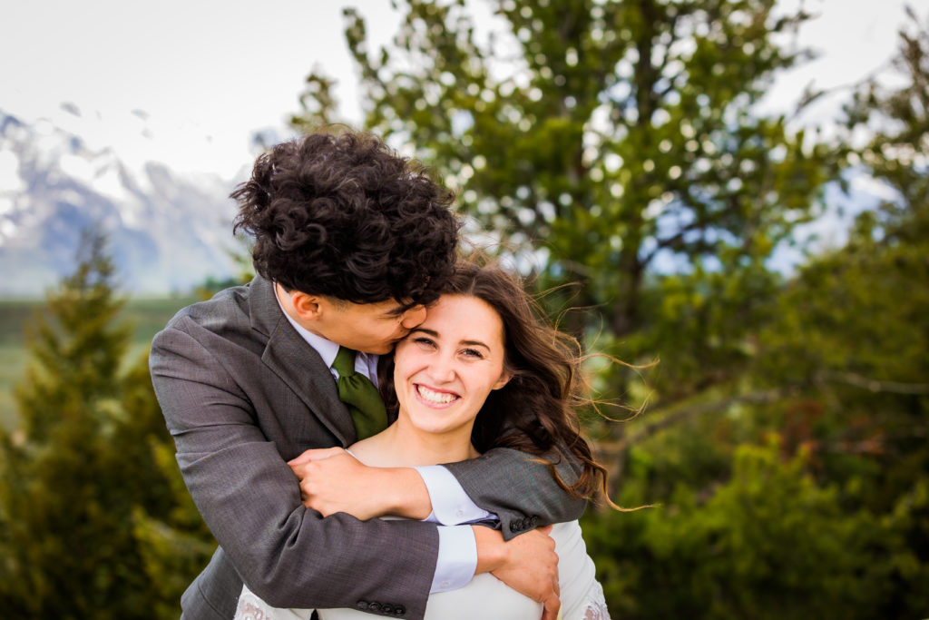groom hugging his bride and kissing her forehead as she smiles for her Grand Teton wedding 