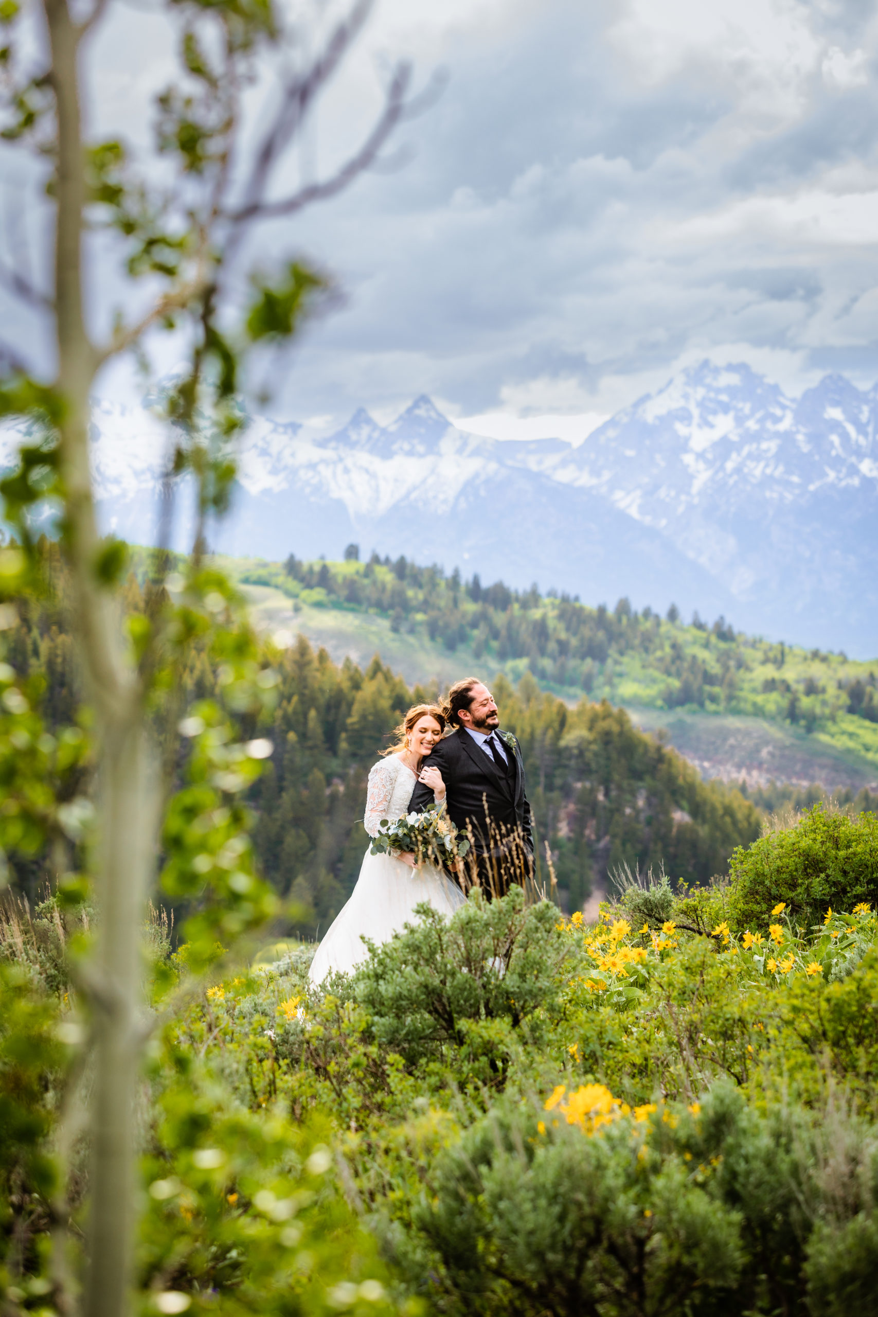 bride hugs groom from behind and groom looks off into the distance at grand teton national park with the tetons for their wedding