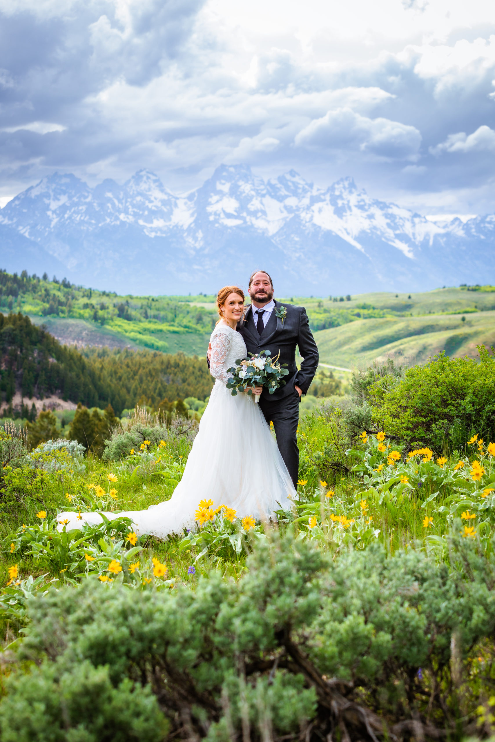 bride and groom surrounded by green grass and wild flowers smile at the camera at their jackson hole wedding at the wedding tree