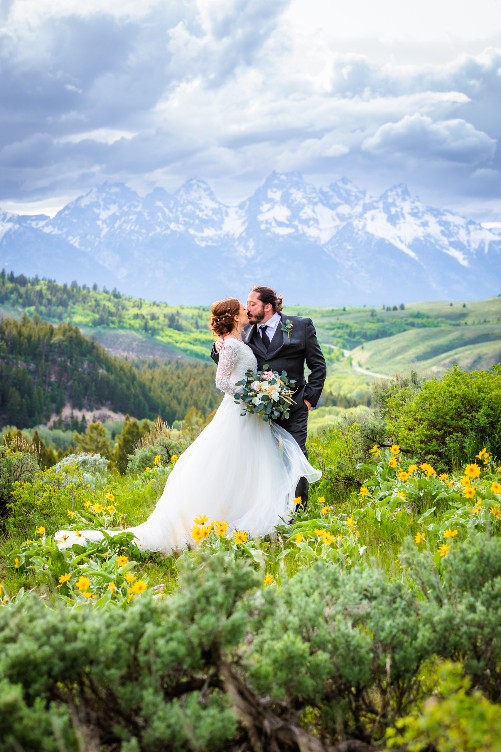 groom and bride kiss as they stand with the tetons as their backdrop