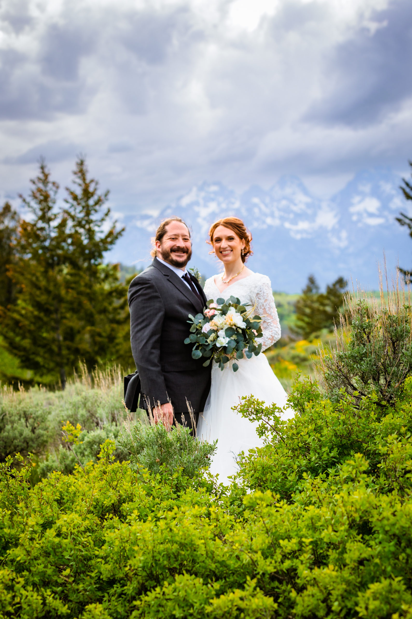 bride and groom standing in tall green grasses with the tetons in the back