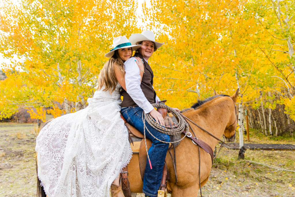 bride and groom sitting on a horse together with the bride holding around the grooms waist