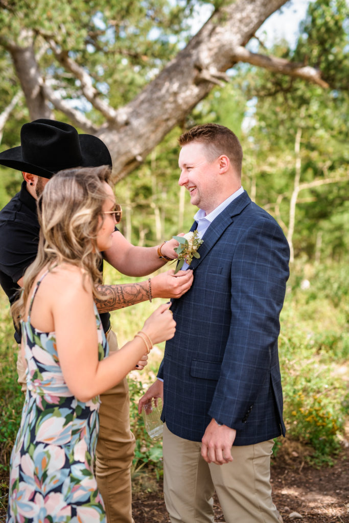 Jackson Hole wedding photographers capture boutonnière being put on groom before wedding tree elopement 