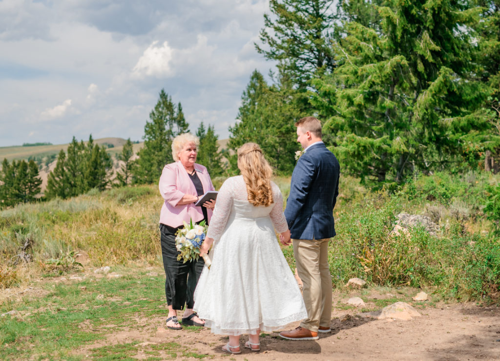Jackson Hole wedding photographer captures couple holding hands in wedding attire during wedding ceremony