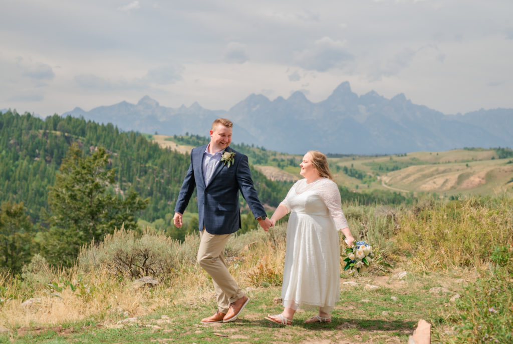 Jackson Hole wedding photographers capture bride and groom holding hands and walking through Grand Teton National Park