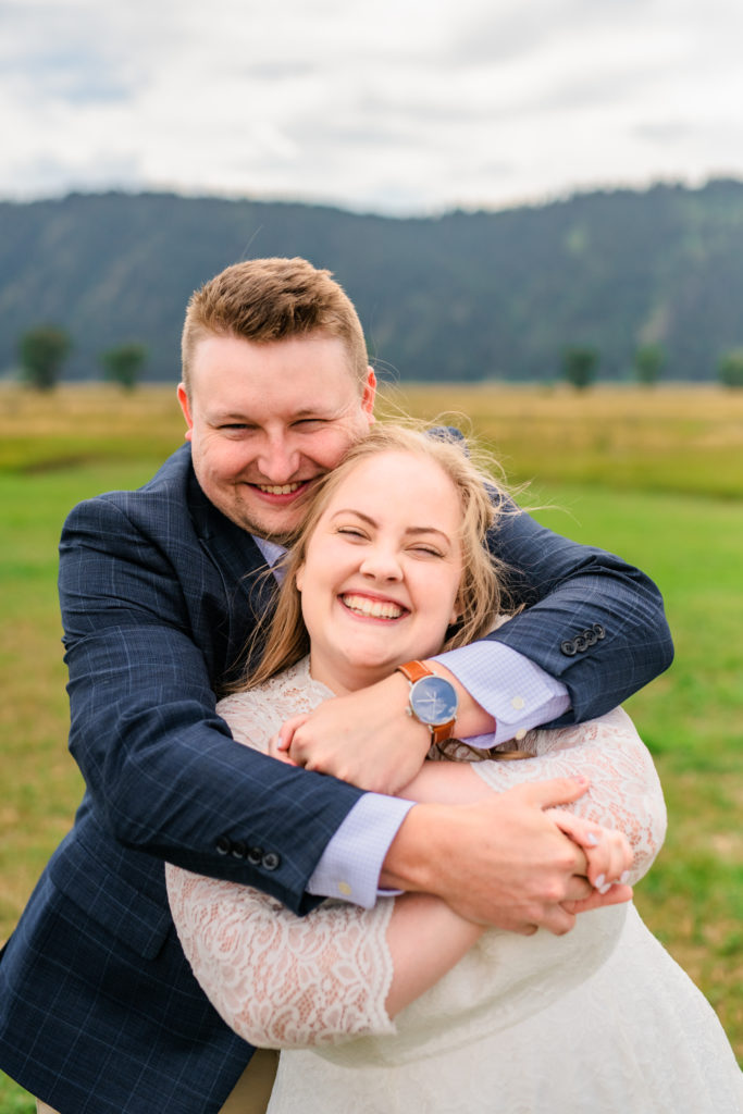 Jackson Hole wedding photographer captures groom hugging bride from behind and smiling really big