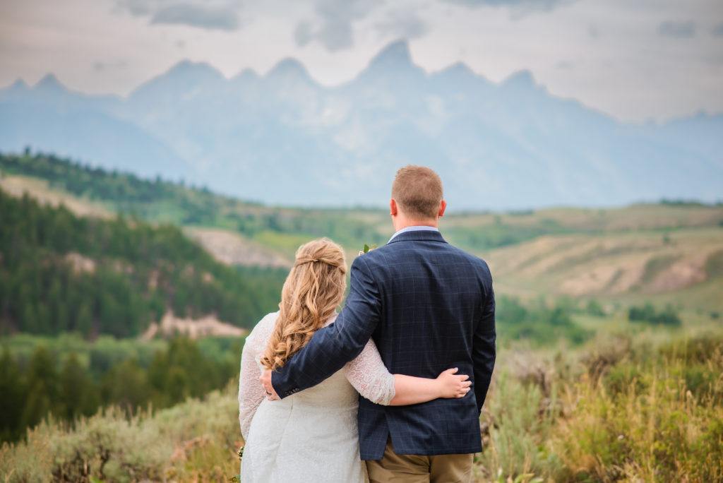 Jackson Hole wedding photographer captures newly married couple with arms around one another looking over mountains