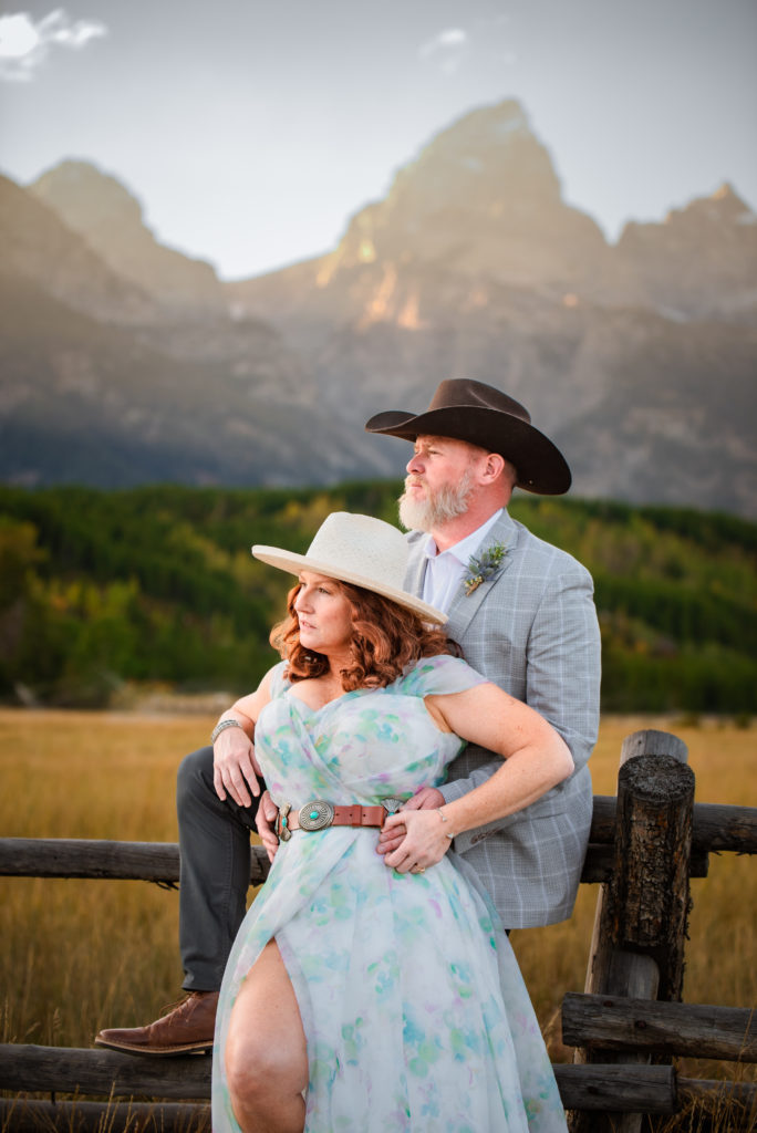 Jackson Hole wedding photographer captures bride and groom leaning against fence during portraits