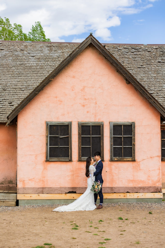 Jackson Hole wedding photographer captures bride and groom standing in front of pink house in mormon row