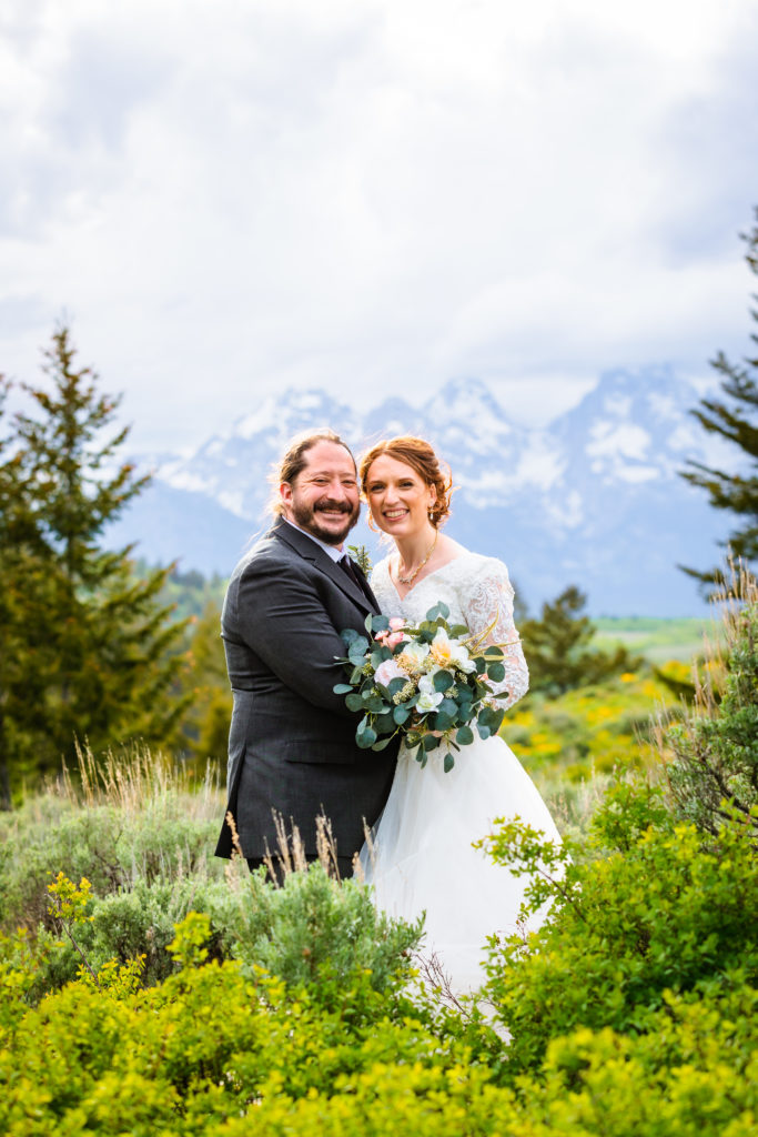 Jackson Hole wedding photographer captures couple embracing in green fields in grand teton national park wedding