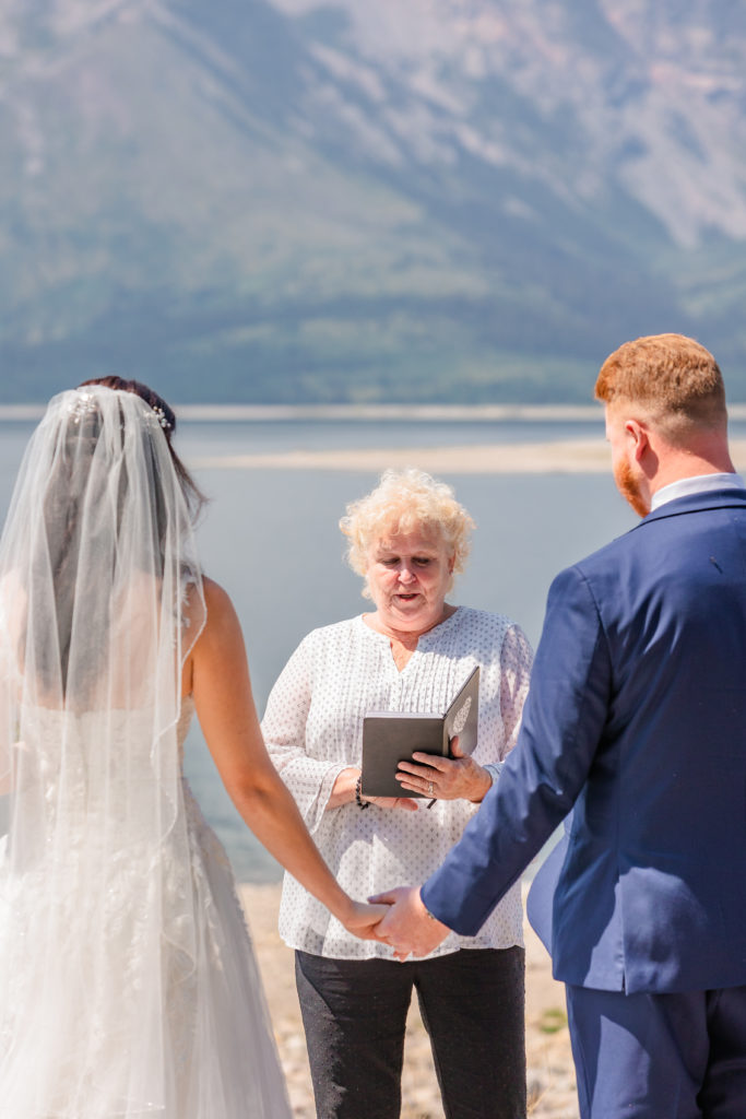 Jackson hole photographers capture bride and groom holding hands while officiant marries them