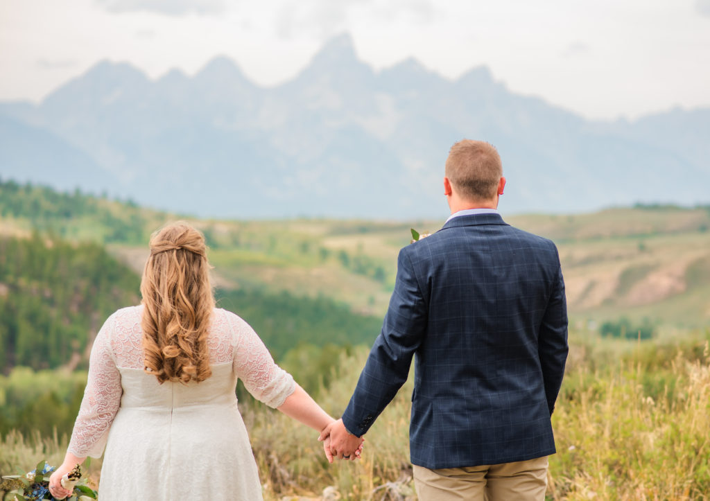 Jackson Hole wedding photographer captures couple holding hands and looking over Tetons