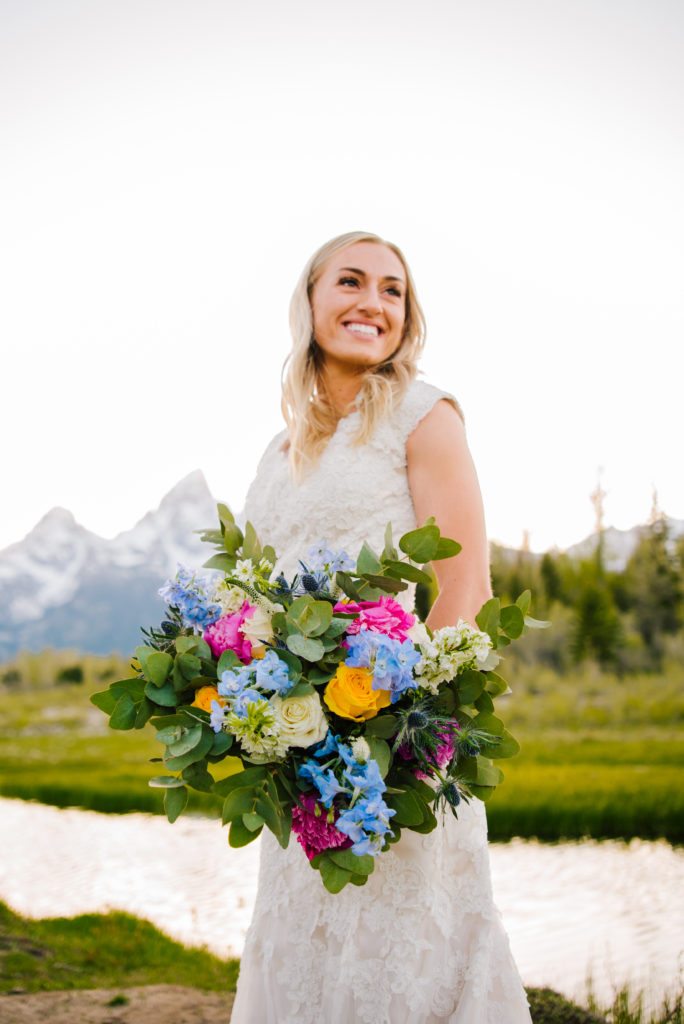Jackson Hole wedding photographer captures bride looking at Tetons holding colorful bridal bouquet