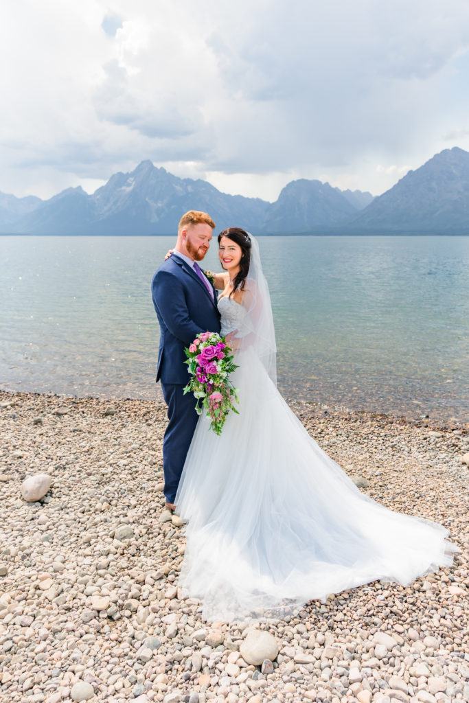 Jackson Hole wedding photographer captures groom wearing a navy suit holding bride wearing strapless wedding gown at colter bay grand teton elopement