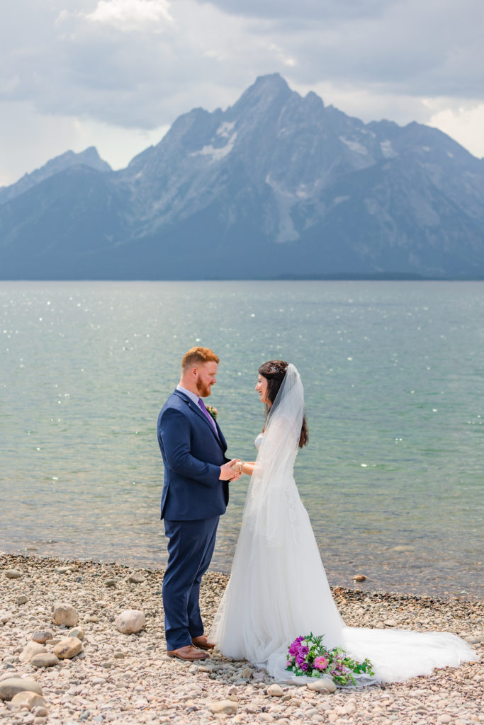 Jackson Hole wedding photographer captures bride and groom wearing wedding attire holding hands in front of Colter Bay
