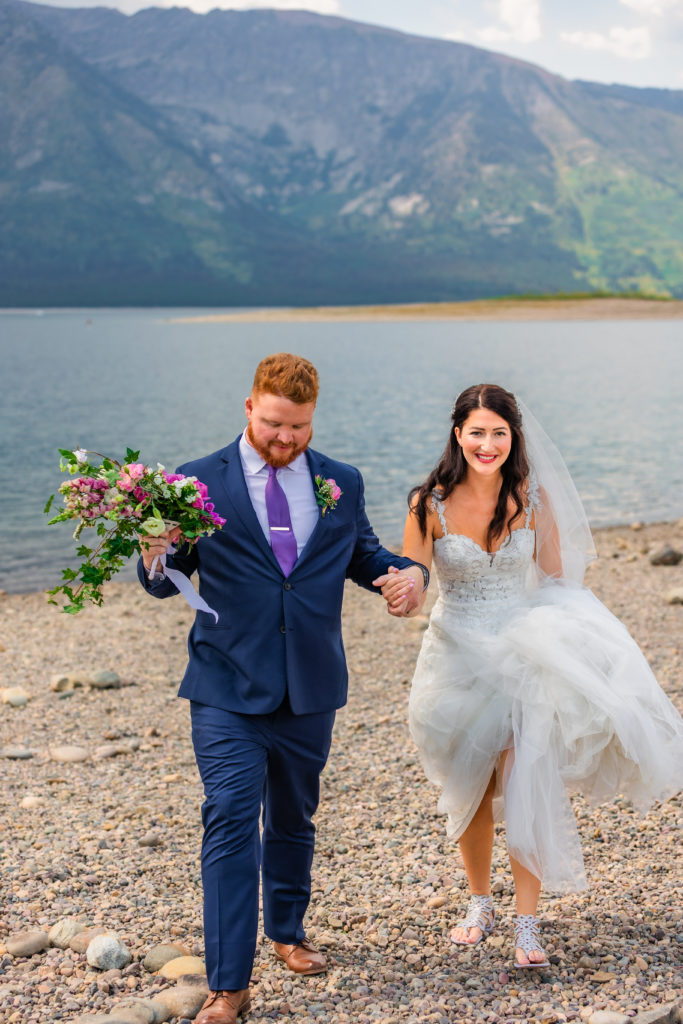 Jackson Hole elopement photographer captures bride and groom wearing wedding attire walking together through Colter Bay