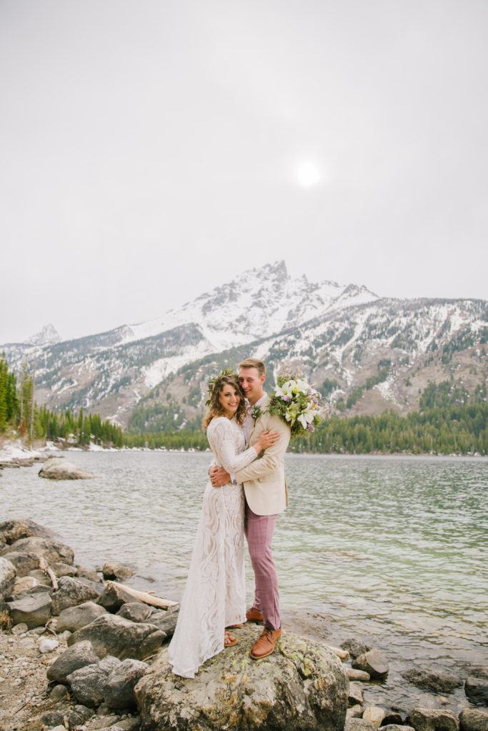 Jackson Hole wedding photographer captures couple standing together at Jenny Lake wearing wedding attire after elopement