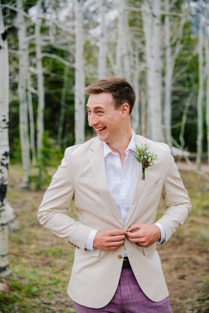 Jackson Hole wedding photographer captures groom buttoning jacket while smiling 