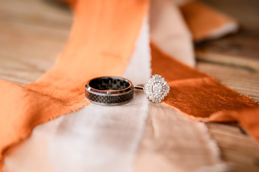 Jackson Hole wedding photographers capture close up details of wedding rings on rust, cream, and orange linen ribbon