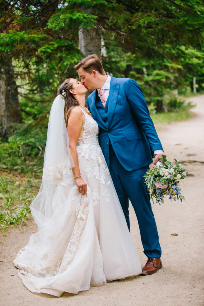 Jackson Hole photographers capture groom wearing blue suit kissing bride in wedding gown during Grand Teton wedding