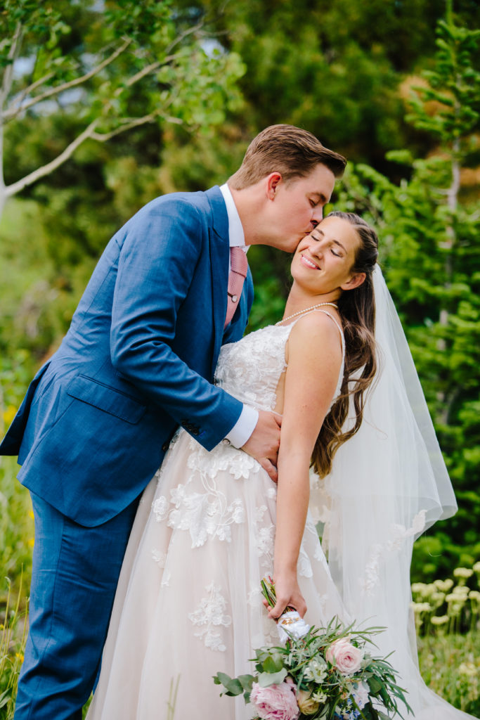 Jackson Hole wedding photographer captures groom kissing bride's cheek during outdoor portraits