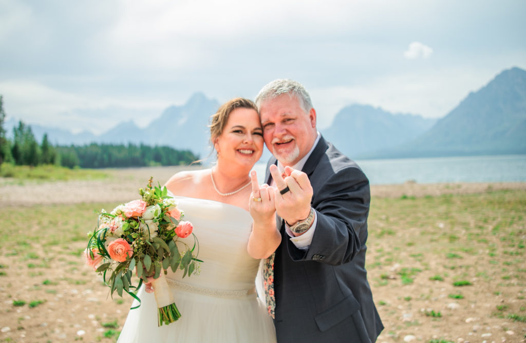 Jackson Hole wedding photographer captures bride and groom holding ring fingers up showing wedding bands after Grand Teton wedding