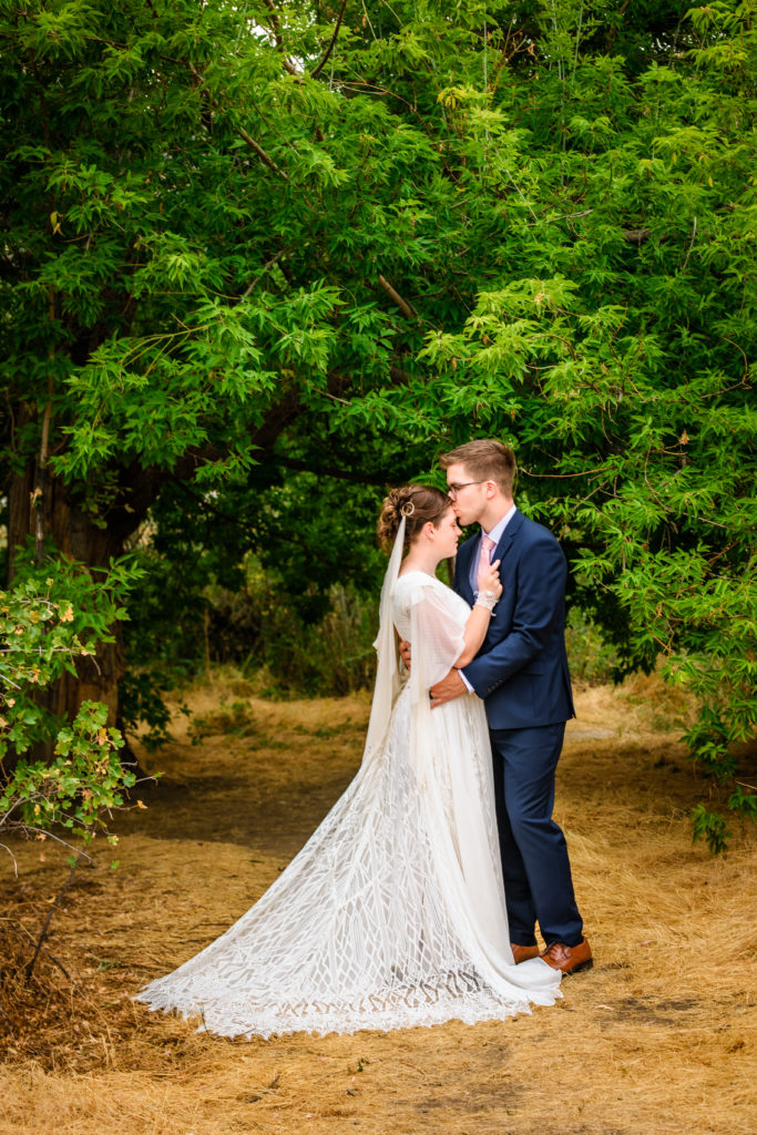 Jackson Hole wedding photographers capture groom wearing blue suit holding bride during outdoor portraits