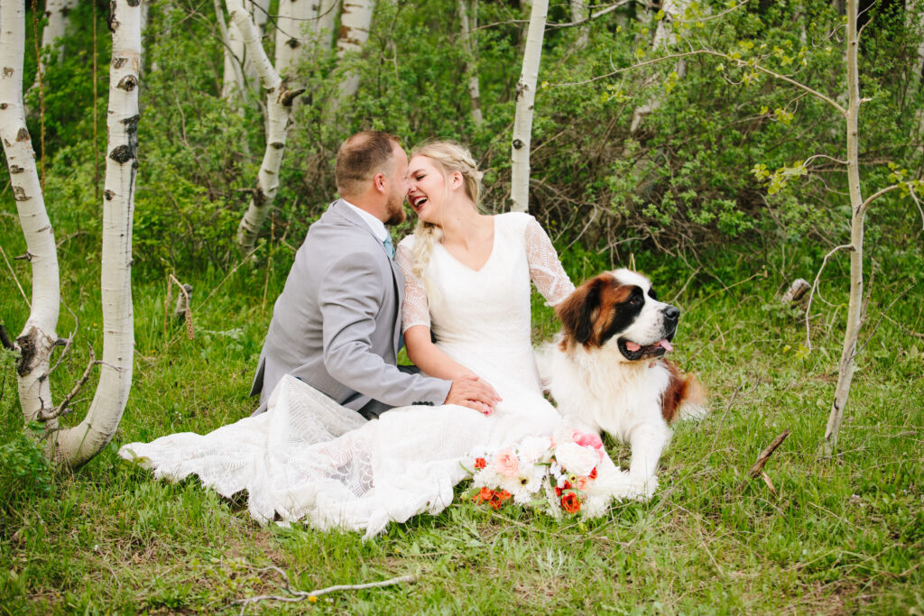 Jackson Hole photographer captures bride and groom sitting with dog in grass after Jackson Hole elopement vendors help with wedding