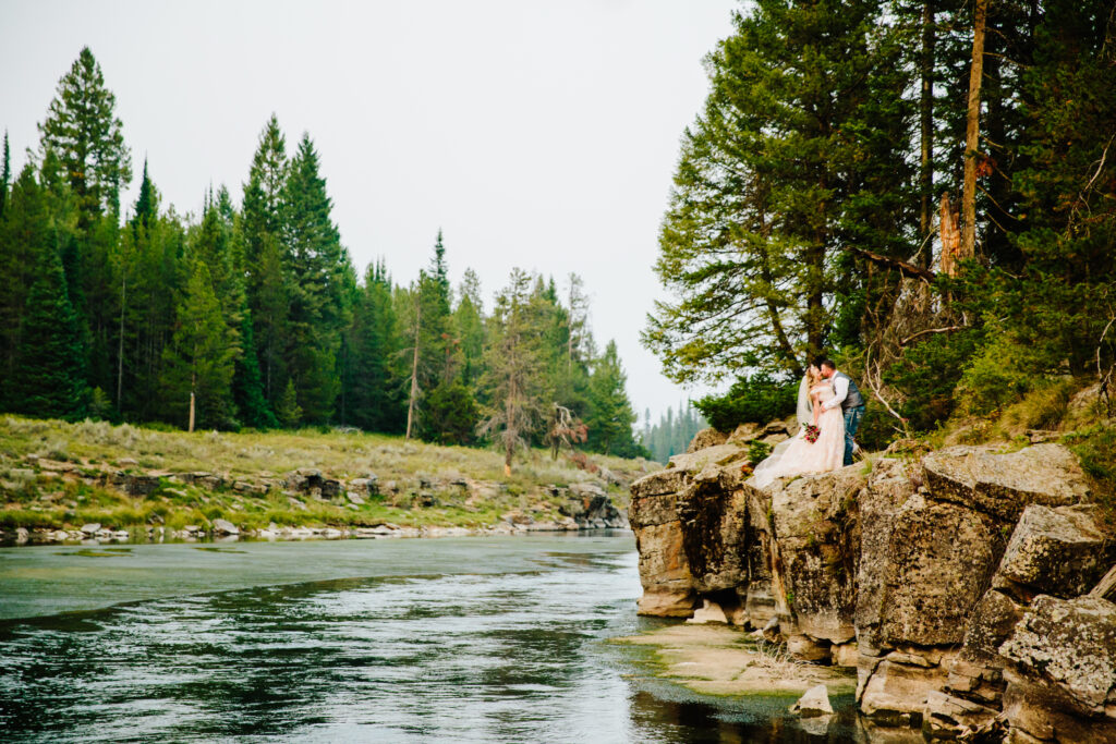 Jackson Hole photographer captures bride and groom kissing alongside water in Grand Teton National Park wedding