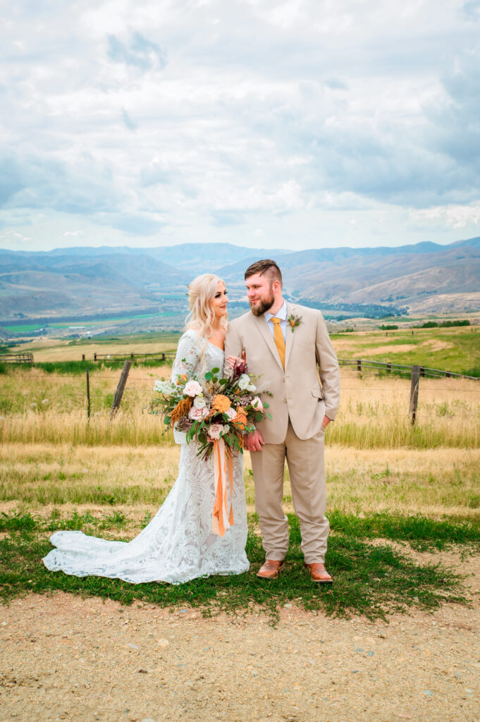 Bride and groom look at each other in posed images while bride holds big orange and cream bouquet with the mountains backdrop behind them