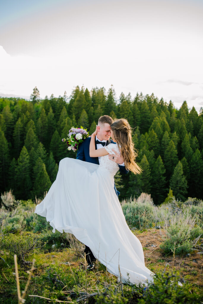 Groom sweeps his bride off her feet after Grand Teton National Park Wedding. They press their heads together and laugh.