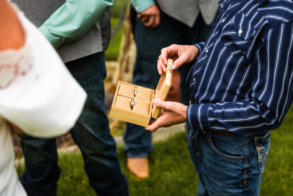 Young boy at wedding opens up box showing wedding rings for both the groom and the bride at grand teton elopement.