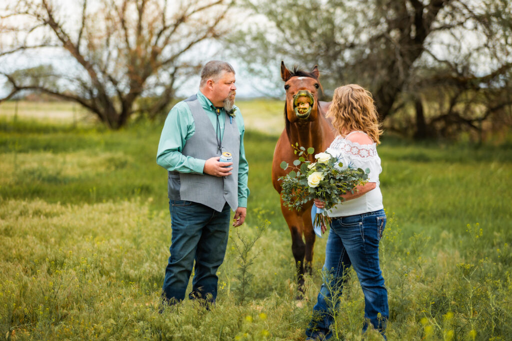 Horse smiles at camera after groom offers it a beer at a grand teton elopement. The bride is wearing a white shirt and jeans while holding flowers.