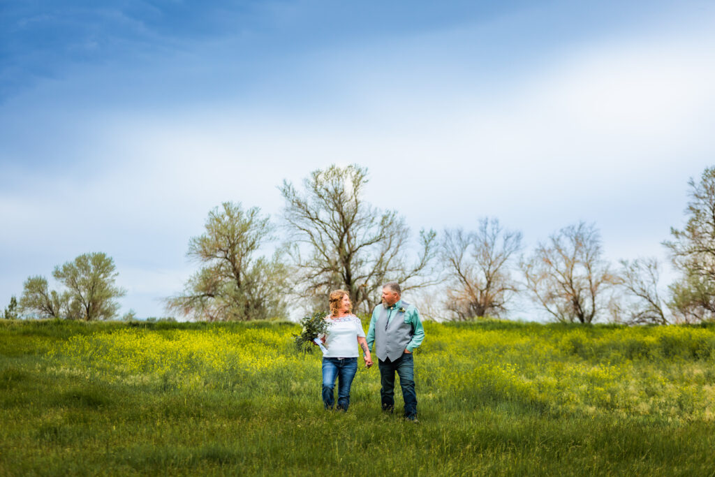 Grand Teton bride and groom walking hand in hand through a flowered field. Bride is wearing a western white shirt and blue jeans.