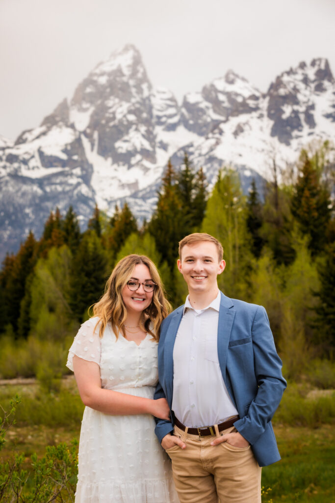 Jackson Hole elopement couple smiles and looks at camera with the tetons behind them. Bride is wearing a swiss dot short white dress.