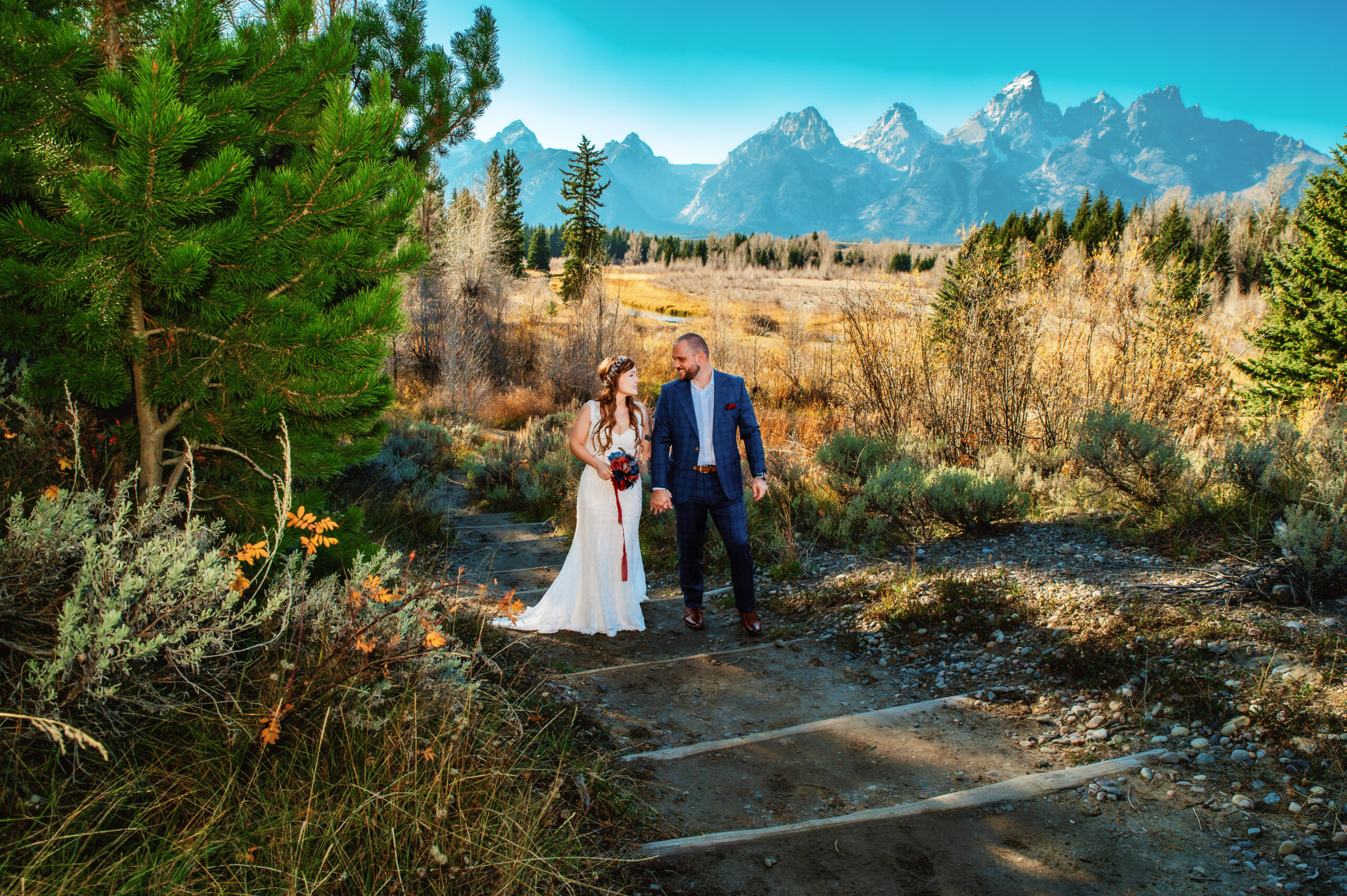 Groom leads bride up staircase at schwbachers landing in grand teton national park during the fall season.