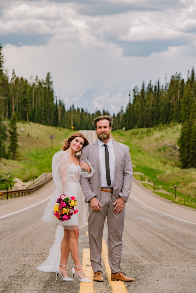 Jackson Hole bride and groom stand in road looking at photographer with the tetons behind them.