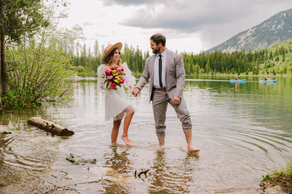 bride and groom walk though Jackson hole lake while smiling at each other at Jackson Hole elopement.
